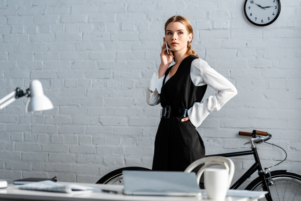confident businesswoman in formal wear talking on smartphone in office - Фото, изображение