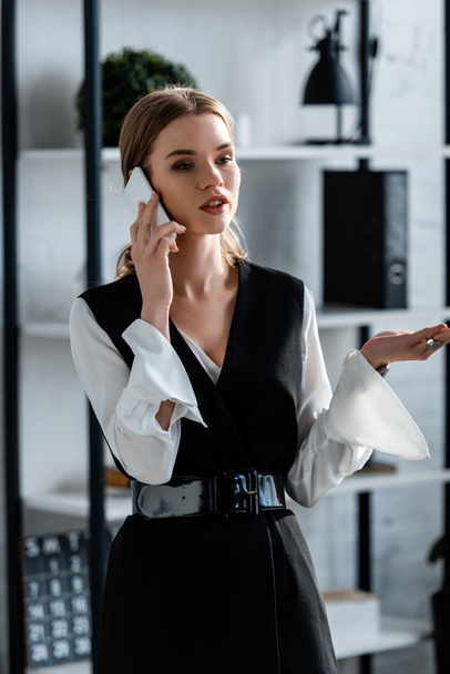 деловая женщина в формальной одежде жестикулируя и разговаривая на смартфоне в офисе
 - Фото, изображение