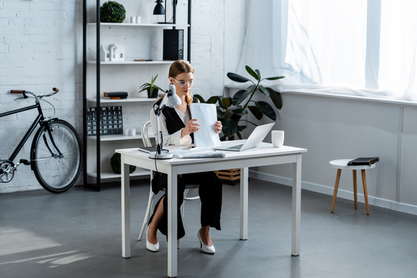 businesswoman in formal wear sitting at computer desk with documents in office - Foto, afbeelding