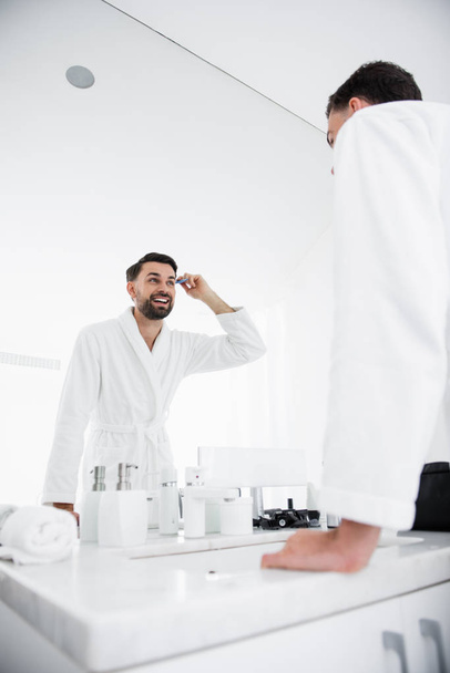 Positive man smiling and combing hair in the bathroom - Foto, Bild