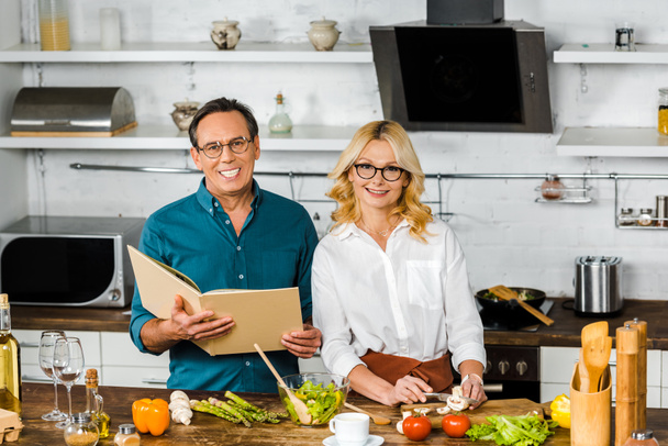 high angle view of mature wife and husband cooking together with recipe book in kitchen - Foto, Imagem