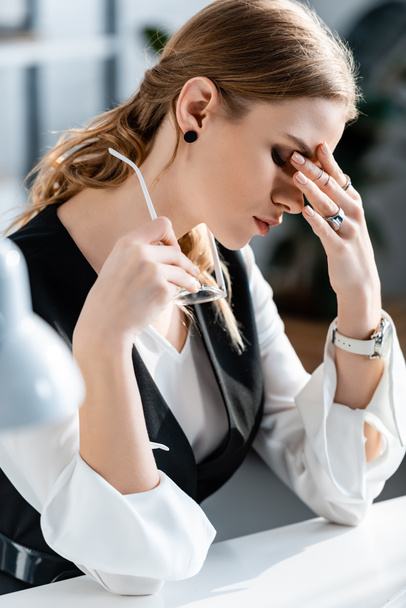 businesswoman in formal wear holding glasses and having headache at workplace - Φωτογραφία, εικόνα