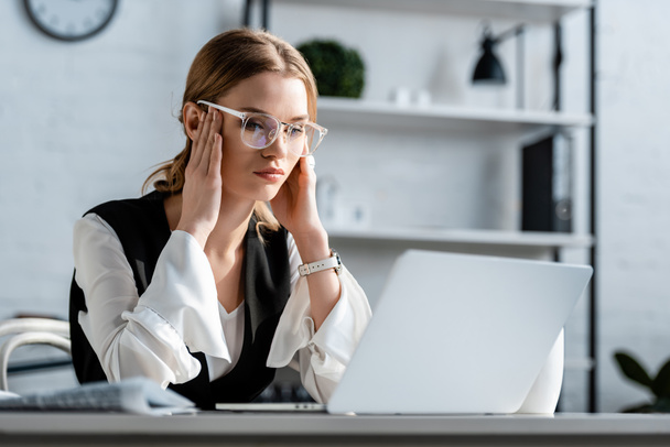 kobieta interesu w wizytowym i okulary, siedząc przy biurku komputer i o ból głowy w miejscu pracy - Zdjęcie, obraz
