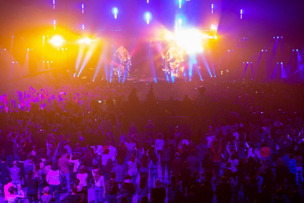 Концертная толпа веселится на рок-концерте. Большой концертный зал с большой сценой. Куча народу. Световое оборудование. Телевидение снимает концерт на нескольких камерах
. - Фото, изображение