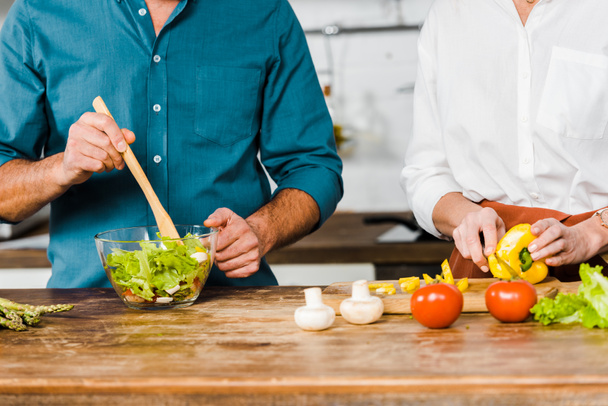 cropped image of mature wife and husband cooking salad together in kitchen - Fotografie, Obrázek