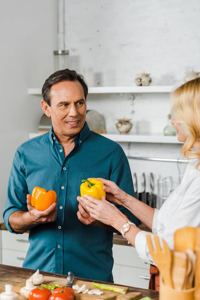 mature wife and husband holding bell peppers for salad in kitchen - Photo, Image