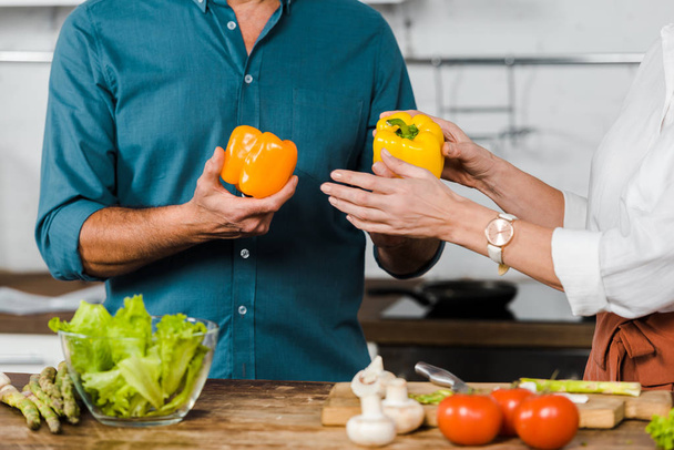 cropped image of mature wife giving bell peppers to husband for cooking salad in kitchen - Fotografie, Obrázek
