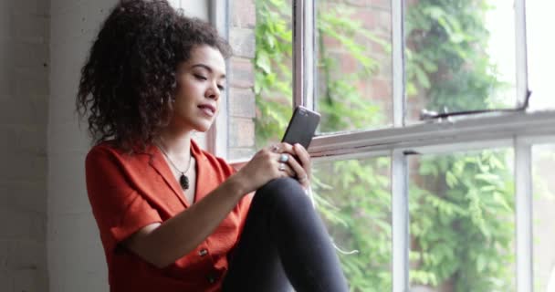Millennial female using smartphone by window in loft apartment - Filmati, video