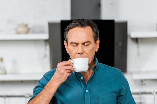 handsome middle aged man drinking tea in kitchen - Fotó, kép