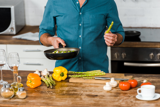 immagine ritagliata di uomo di mezza età che cucina verdure sulla padella in cucina
 - Foto, immagini