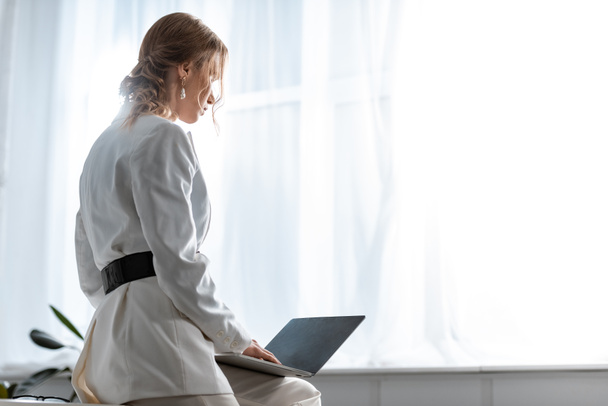 Achteraanzicht van zakenvrouw in witte formele slijtage met behulp van laptop op werkplek met kopie ruimte - Foto, afbeelding