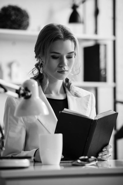 Schwarz-Weiß-Foto einer Geschäftsfrau in offizieller Kleidung, die am Schreibtisch sitzt und am Arbeitsplatz Notizbücher liest - Foto, Bild