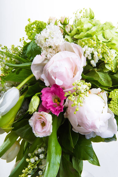 A large number of yety, a large lush bouquet of snowdrop, rose, bell and peony with greens in a large long stylish transparent vase on the leg on a white isolate background. - Foto, Imagem