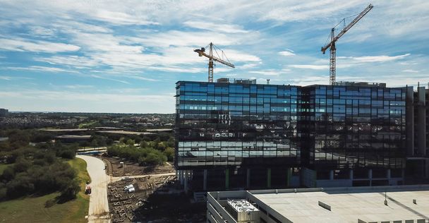 Panorama luchtfoto werkende kraan op de bouwplaats van nieuwe zakelijke gebouw hoogbouw en parkeergarage met meerdere artikelen - Foto, afbeelding