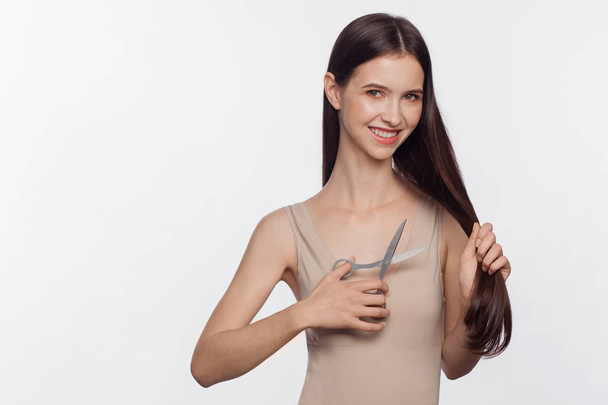 Portrait of beautiful young woman cuts off her hair by scissors - Foto, imagen