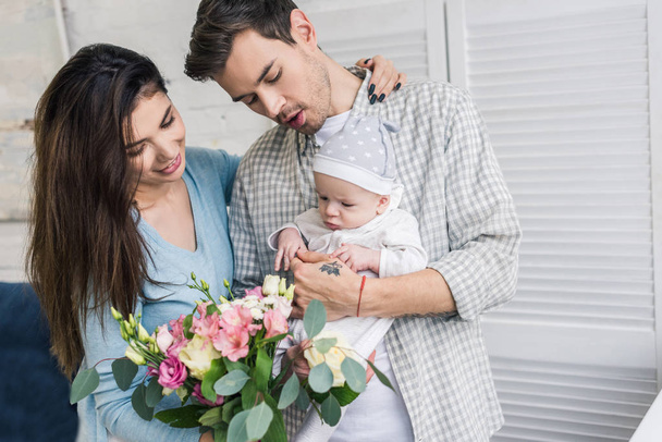 retrato de padres felices con hijo pequeño y ramo de flores en casa
 - Foto, imagen