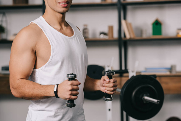 cropped view of muscular bi-racial man exercising with dumbbells  - Foto, afbeelding