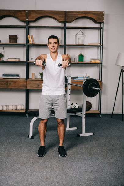 handsome bi-racial man exercising with dumbbells in living room  - Photo, image