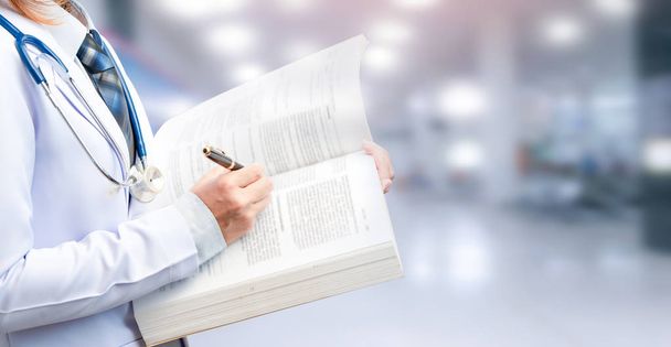 woman doctor holding textbook and pointing to important content on blurred patient department of hospital  - Фото, изображение