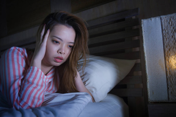 young beautiful sad and depressed Asian Chinese girl lying on bed late night awake looking thoughtful suffering insomnia sleeping disorder feeling tired and worried in woman depression concept - 写真・画像