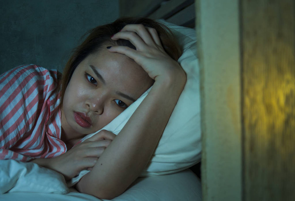 young beautiful sad and depressed Asian Chinese girl lying on bed late night awake looking thoughtful suffering insomnia sleeping disorder feeling tired and worried in woman depression concept - Foto, imagen