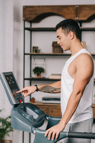 handsome bi-racial man pushing sensor button on control panel of  treadmill  - Foto, Imagem
