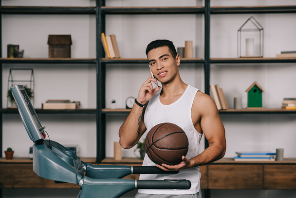 handsome bi-racial sportsman talking on smartphone and holding basketball  - Foto, Imagem