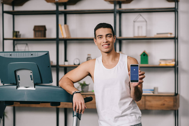 cheerful bi-racial man holding smartphone with facebook app on screen   - Photo, Image