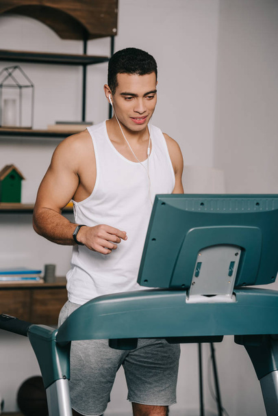  mixed race man exercising on treadmill and listening music in earphones  - Foto, afbeelding