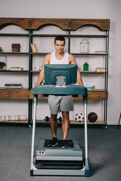 cheerful muscular bi-racial man exercising on treadmill in living room - Fotografie, Obrázek