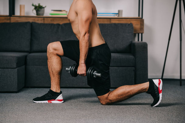 cropped view of man doing lunges exercise with dumbbell near sofa  - Foto, Bild