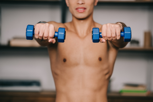 cropped view of mixed race man exercising with blue dumbbells  - Fotografie, Obrázek