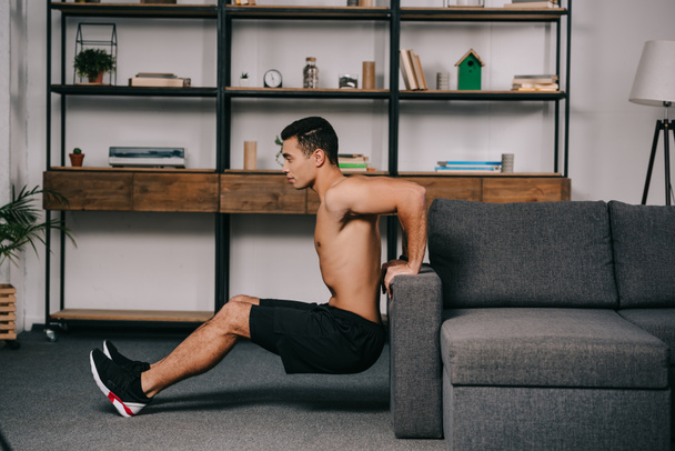 handsome mixed race man workout near sofa in living room  - Fotó, kép