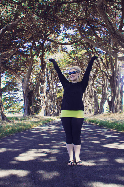 Blonde female raises arms up at the Cypress Tree Tunnel on Point Reyes National Seashore in Marin County in Northern California - Photo, Image