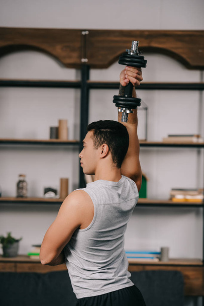 сильный бирасовый мужчина тренируется с гантелями в гостиной
  - Фото, изображение