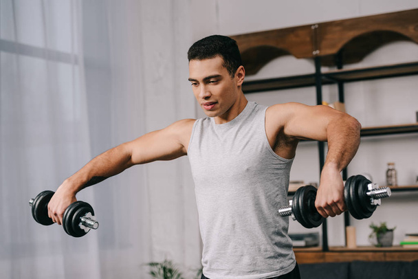handsome bi-racial man doing exercise with dumbbells in living room  - Foto, immagini