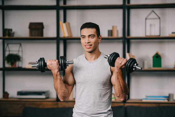 smiling mixed race man workout with dumbbells in living room  - Foto, Imagem