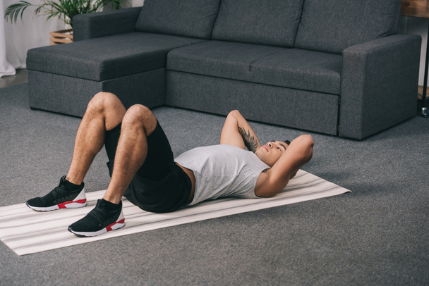 tattooed bi-racial man lying on fitness mat and doing exercise - Foto, Imagem