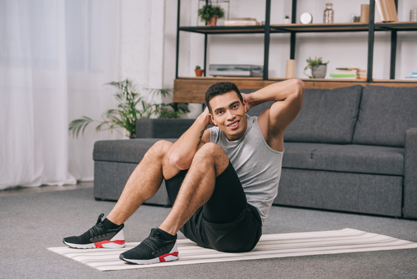 handsome bi-racial man sitting on yfitness mat and doing exercise - Foto, immagini