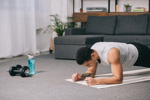 hombre bi-racial haciendo ejercicio de tablón en la alfombra de fitness en el apartamento
  - Foto, Imagen