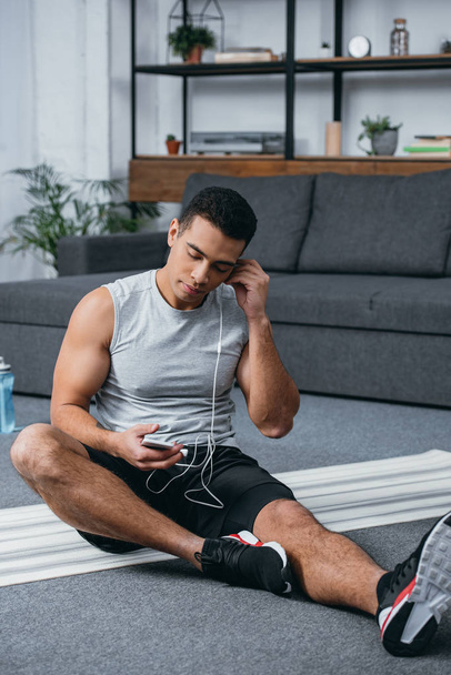 bi-racial man holding smartphone and listening music in earphones with closed eyes - Фото, изображение