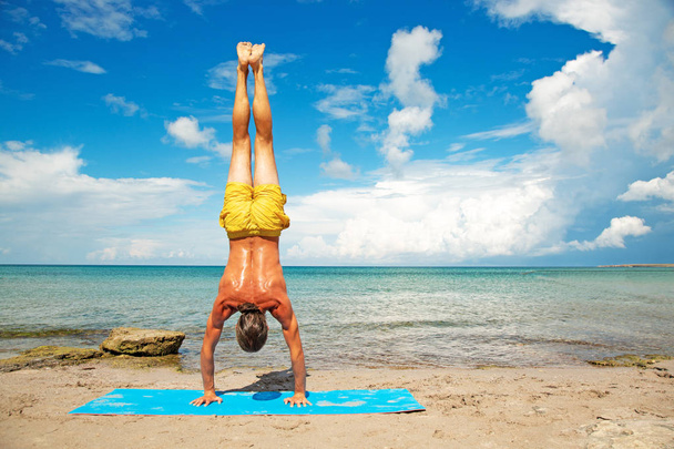 sportos férfi csinál jóga edzés strandon. Acroyoga elem erő és egyensúly. - Fotó, kép