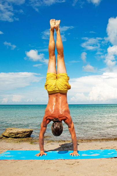 lekkoatletycznego mężczyzna na plaży robi ćwiczenia jogi fitness. Element Acroyoga dla siły i równowagi. - Zdjęcie, obraz