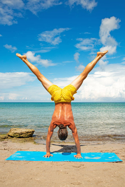 athletic man on beach doing fitness yoga exercise. Acroyoga element for strength and balance. - 写真・画像