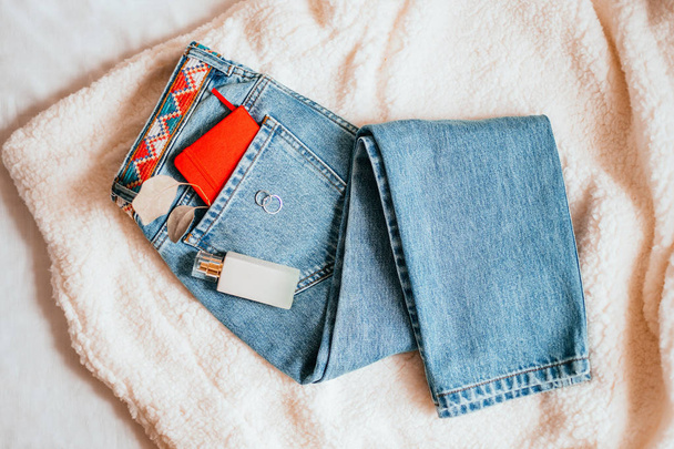Gezellige mode flatlay met blue jeans, rode laptop, parfumfles en accessoires. Minimalistische flatlay op het bed. - Foto, afbeelding