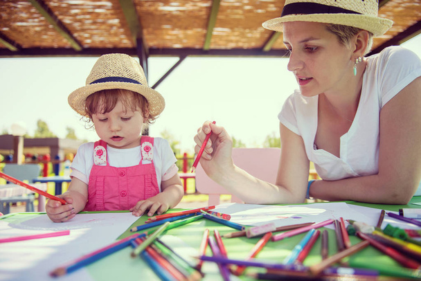 Genç Anne ve onun küçük kızı neşeyle harcama zaman içinde dış anaokulu renkli resimler çizerken kalem boya kalemleri kullanarak birlikte - Fotoğraf, Görsel