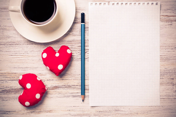 Coffee cup notepad pencil and two red hearts on wooden surface - Photo, Image