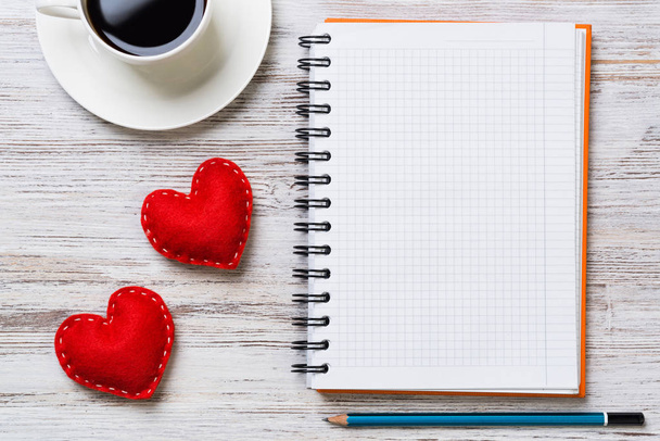 Coffee cup notepad pencil and two red hearts on wooden surface - Foto, imagen