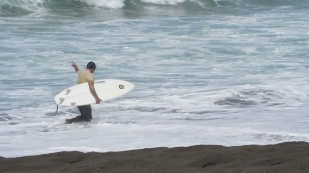 Junger Surfer am Strand mit seinem Surfbrett unter dem Arm. Surfer bereit, in der Karibik auf den Wellen zu surfen.Wassersport-Videos in Superzeitlupe. - Filmmaterial, Video