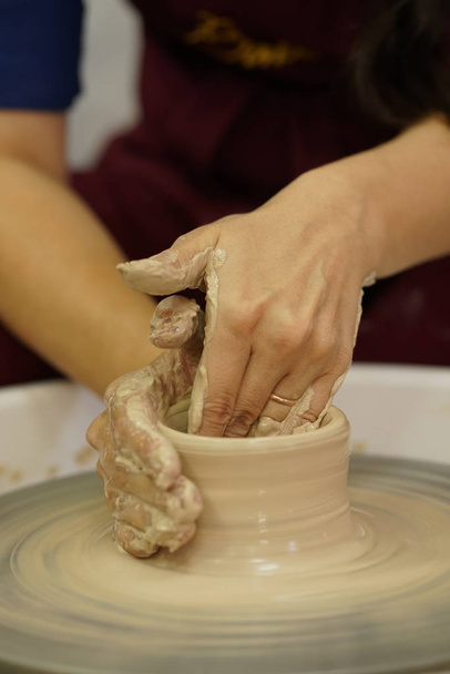 Frau fertigt Krug mit schmutzigen Armen auf Töpferscheibe aus rohem, feuchtem Ton - Foto, Bild